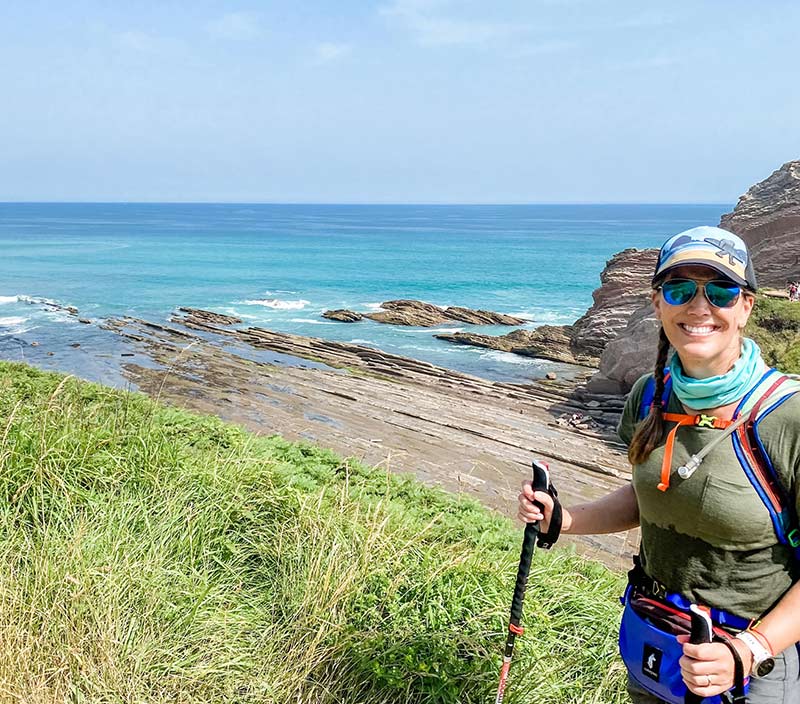 Hiker smiling in front of sea and rock formations.